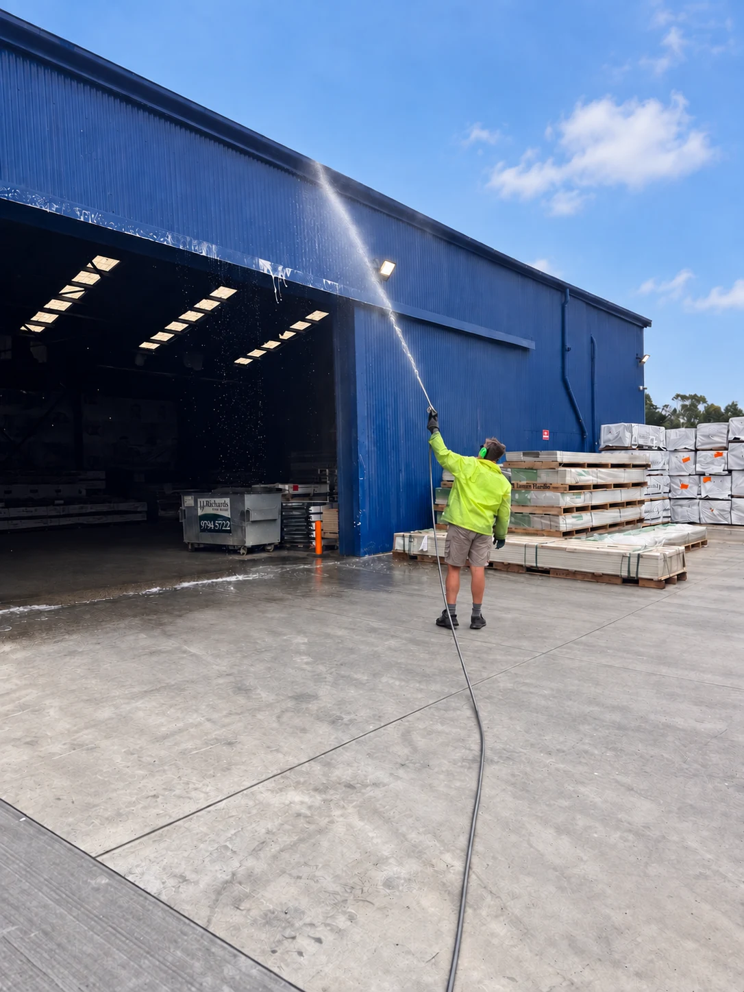 Soft washing a warehouse wall beside stacked materials